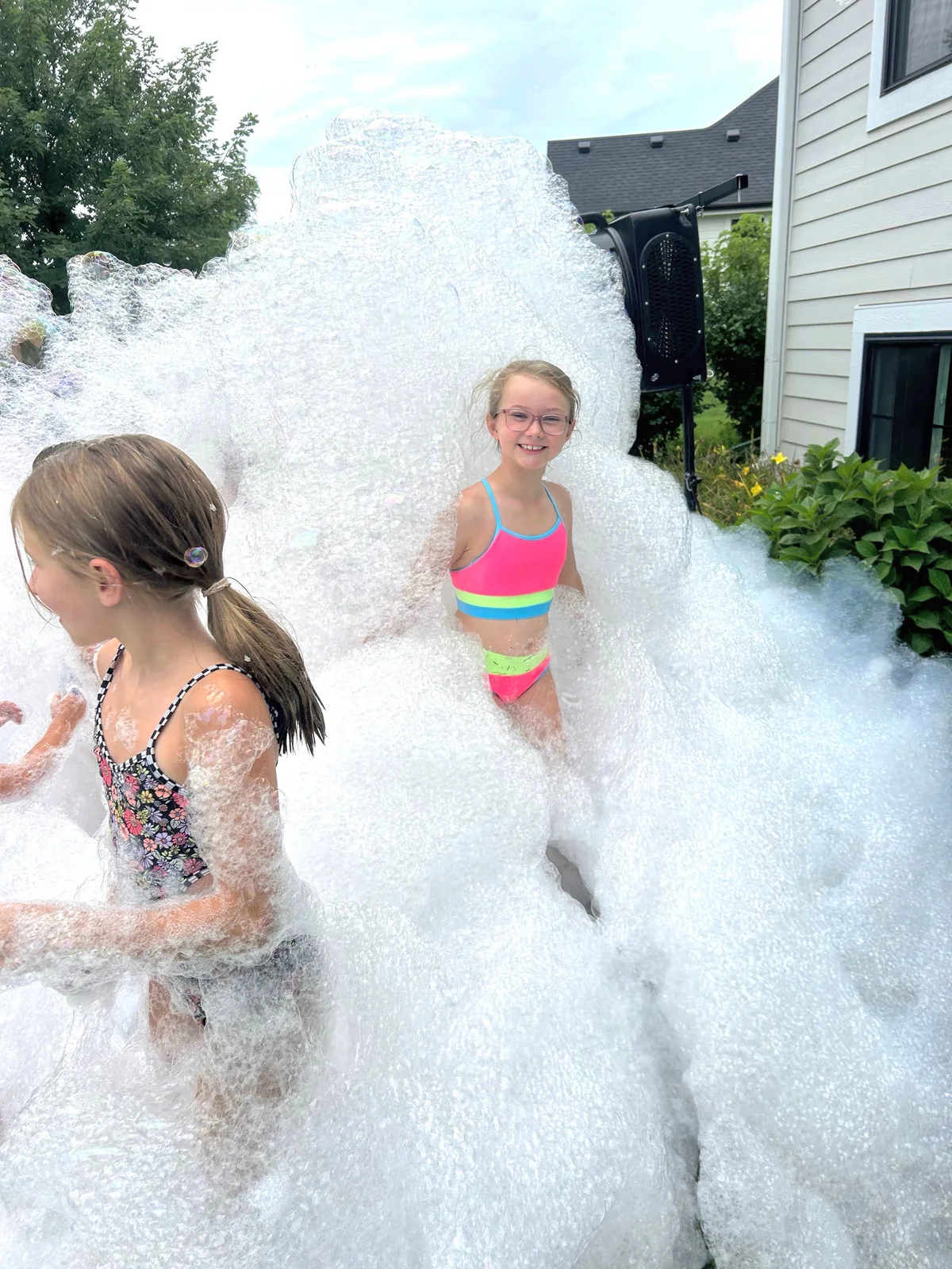 Kids enjoying a backyard foam party beside a professional foam machine
